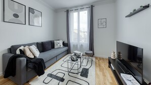A modern living room with a grey sofa, a coffee table, a flat-screen TV, and a bookshelf. - House 8 persons - Subway + train station / Private parking lot / Wifi / CDG airport / (La Courneuve)