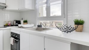 A modern kitchen with white cabinetry, a stainless steel sink, and a window with blinds. - House 8 persons - Subway + train station / Private parking lot / Wifi / CDG airport / (La Courneuve)