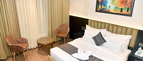 A hotel room with a bed, two armchairs, a small table, a painting, and a nightstand.