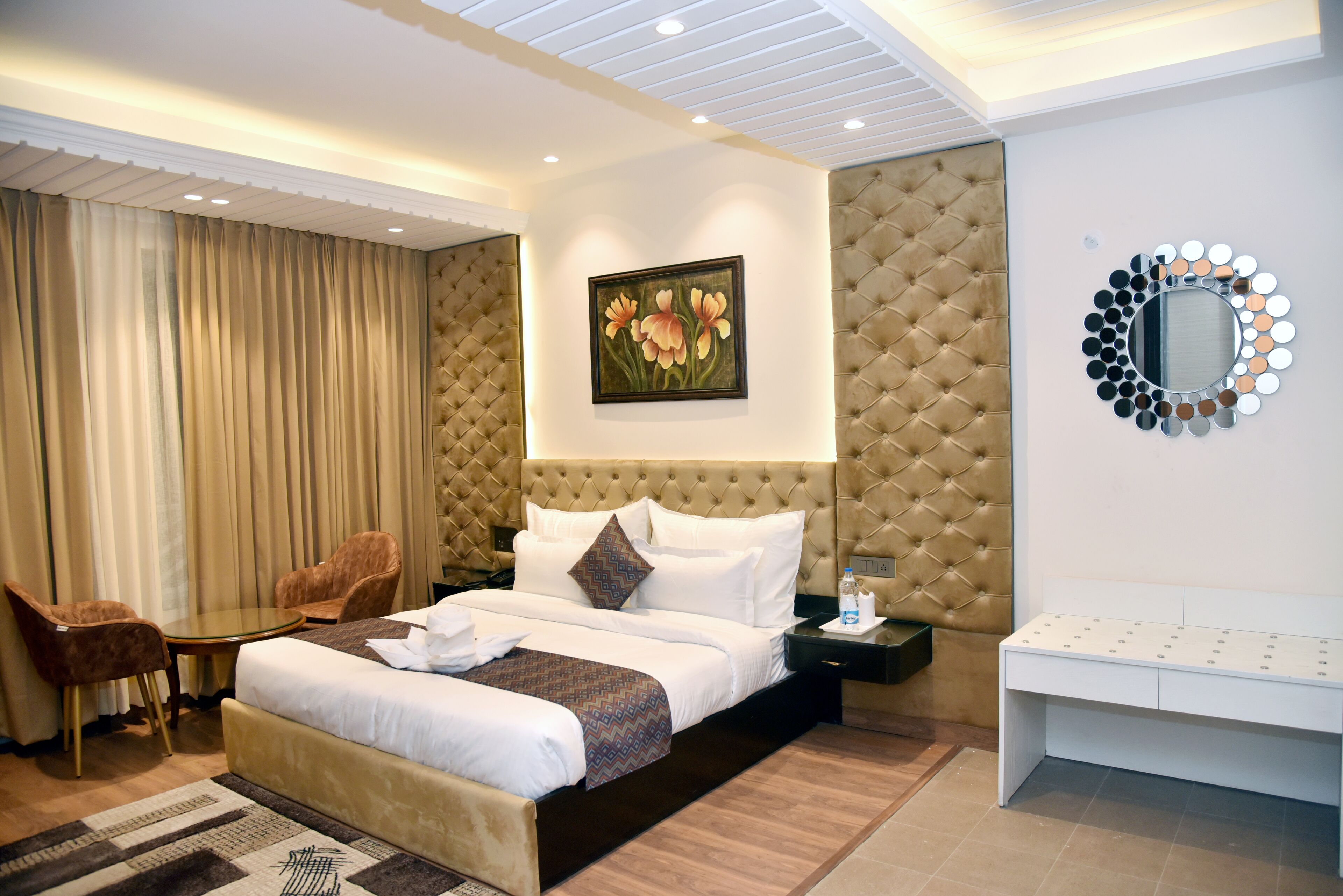 Habitación de hotel con una cama grande, cabecera capitonada, espejo redondo, un cuadro, un escritorio y una silla.