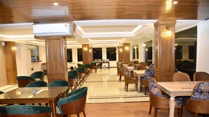 Un comedor amplio con suelo de madera y una mesa central con superficie de vidrio, rodeada de sillas tapizadas.