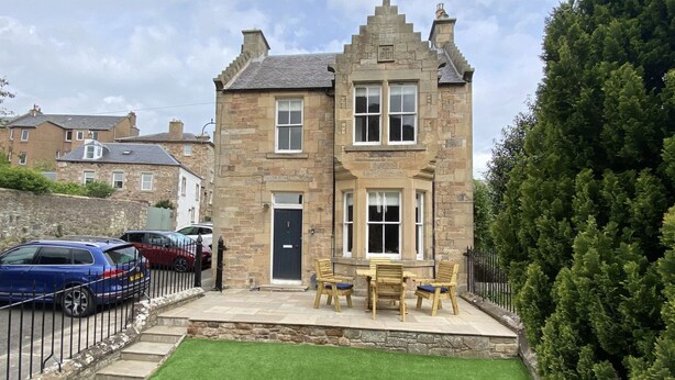 A stone building with a black door, a small front porch with a bench and table, and a well-maintained lawn. - Abbey House, charming traditional historic house. Spectacular views of the Abbey (Jedburgh)