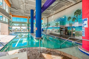 An indoor swimming pool with clear water, surrounded by blue pillars and a mural of a beach scene. - FUN AND SUN IN 801 Ocean Views, Resort Amenities (Myrtle Beach)