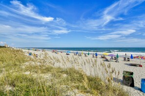 Ein Strand mit Reihen von Liegestühlen und Sonnenschirmen, ein sandiger Uferstreifen und das Meer im Hintergrund.