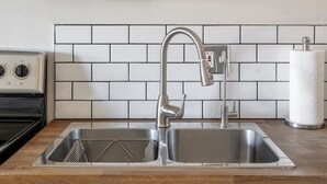 A kitchen with a stainless steel sink, a wooden countertop, a white tiled backsplash, and a wall-mounted light fixture. - Bright 4BR Getaway – Yard & Perfect Group Escape! (Tucson)