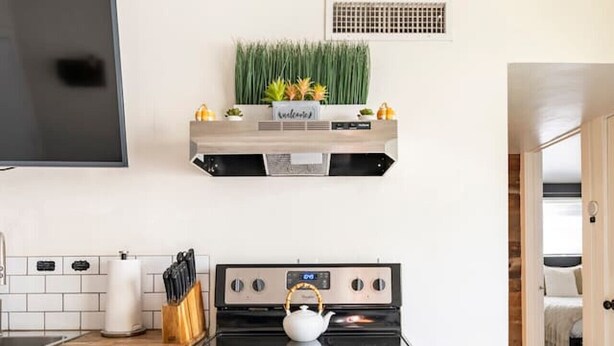 A kitchen with a stainless steel stove, a flat-screen TV above it, and a small refrigerator to the left. - Bright 4BR Getaway – Yard & Perfect Group Escape! (Tucson)