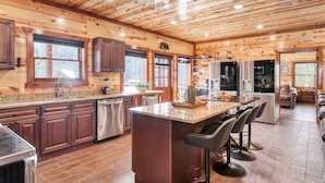 Une cuisine spacieuse dotée de meubles en bois, d’un grand îlot central avec des tabourets, d’appareils électroménagers en acier inoxydable et offrant une vue sur l’extérieur.