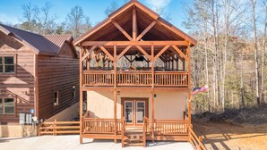 Une cabane en bois à deux étages, dotée d’un balcon, d’un drapeau et offrant une vue sur la forêt environnante.