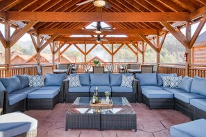 Un patio techado al aire libre con un sofá seccional grande, una mesa de centro de vidrio y un ventilador de techo.
