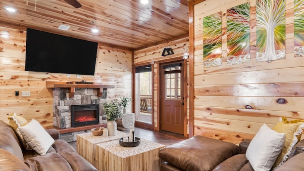 Un intérieur de chalet chaleureux avec une cheminée en pierre, des canapés en cuir et un téléviseur fixé au mur.