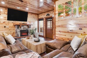 Un intérieur de chalet chaleureux avec une cheminée en pierre, des canapés en cuir et un téléviseur fixé au mur.