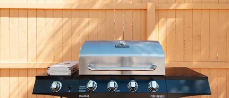 Ein Char-Broil Performance Grill mit vier Brennern und einer Seitablage vor einem Holzzaun.