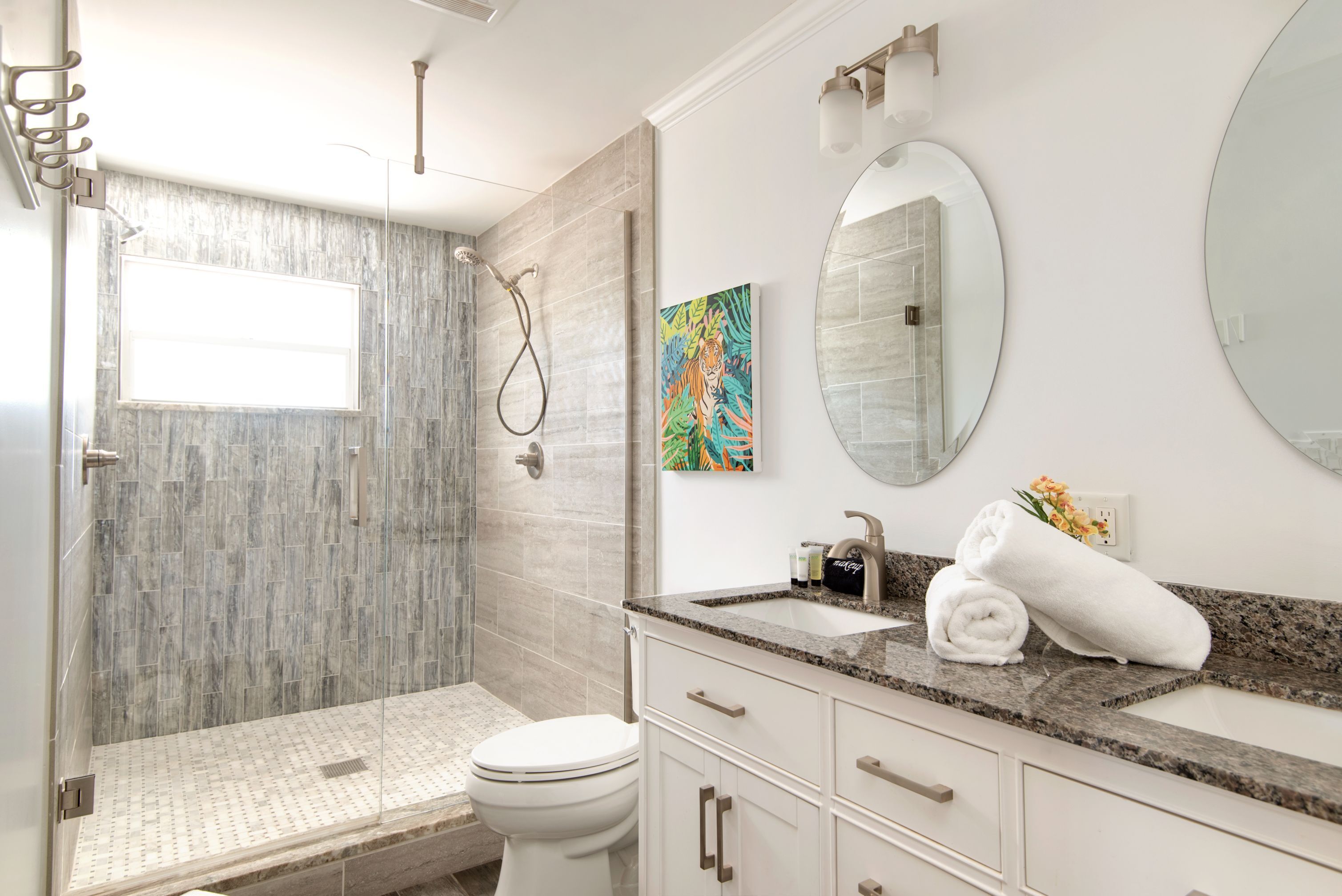 A modern bathroom with a walk-in shower, a toilet, a sink with a granite countertop, and a large mirror.