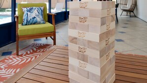 Una stanza con una ventola a soffitto, una pila di blocchi Jenga, una sedia verde con un cuscino blu e una sedia in vimini.