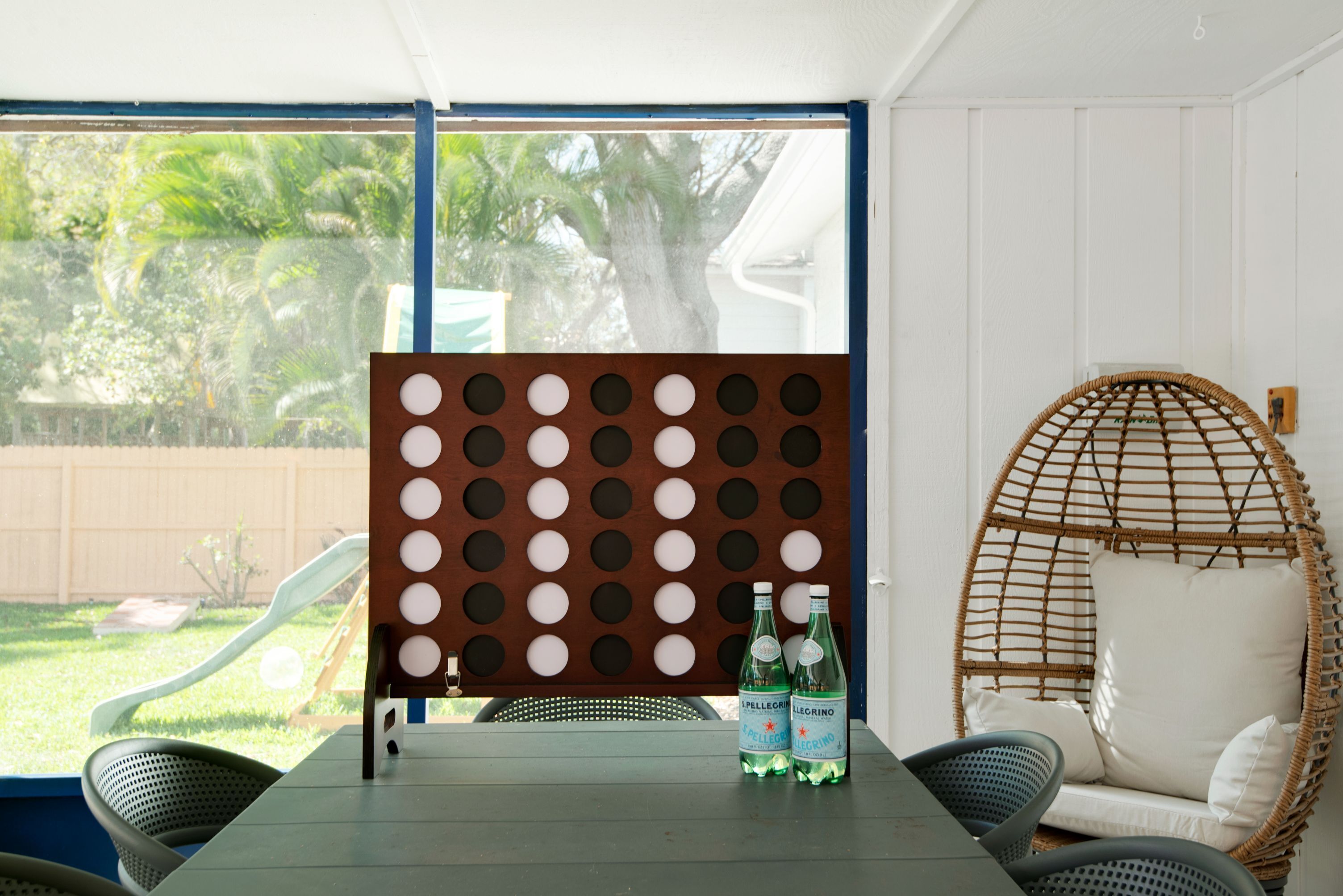 Une pièce avec une table, des chaises, un fauteuil en osier et des bouteilles posées sur la table.