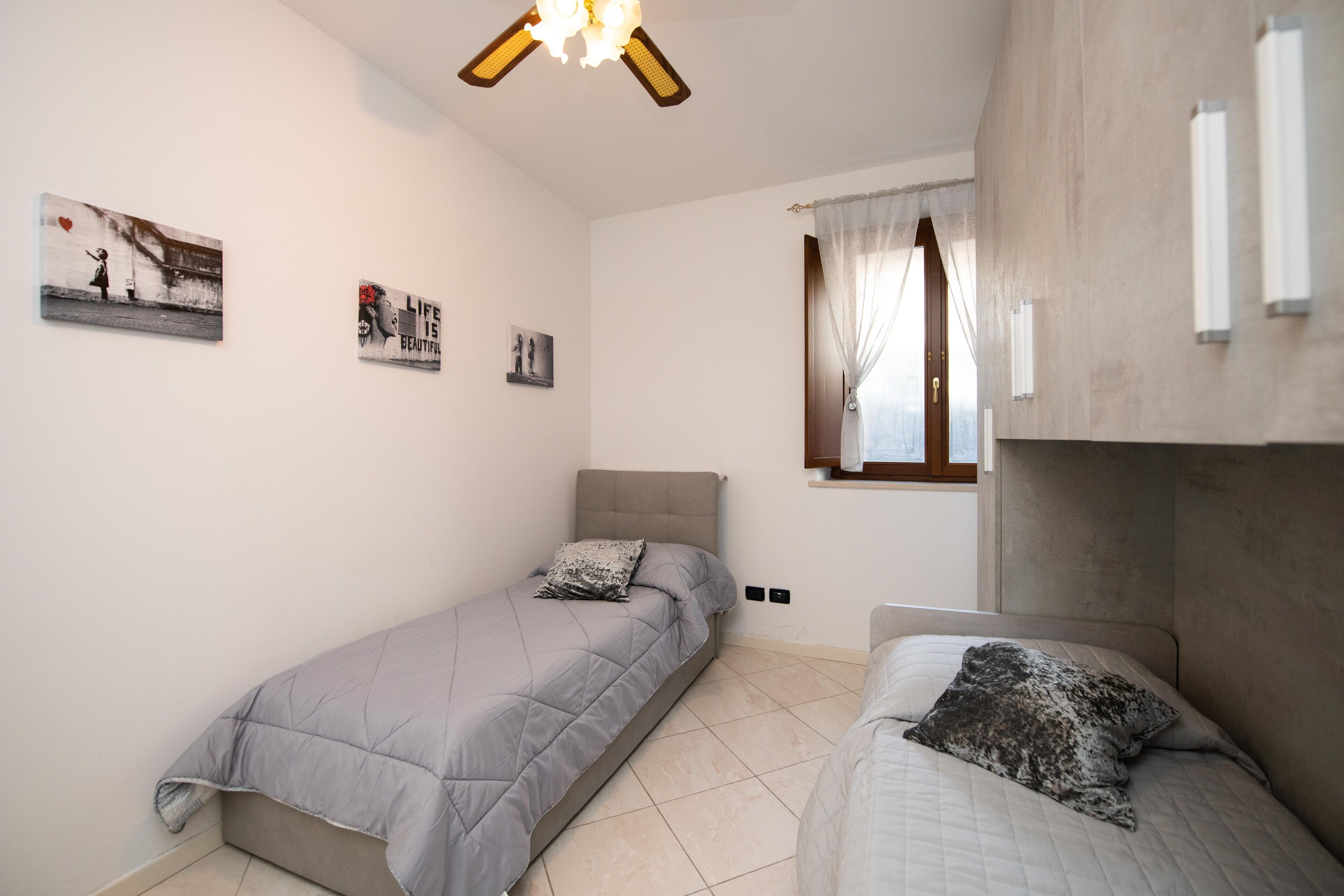 Une chambre avec deux lits simples, un ventilateur de plafond et des œuvres d’art accrochées aux murs.