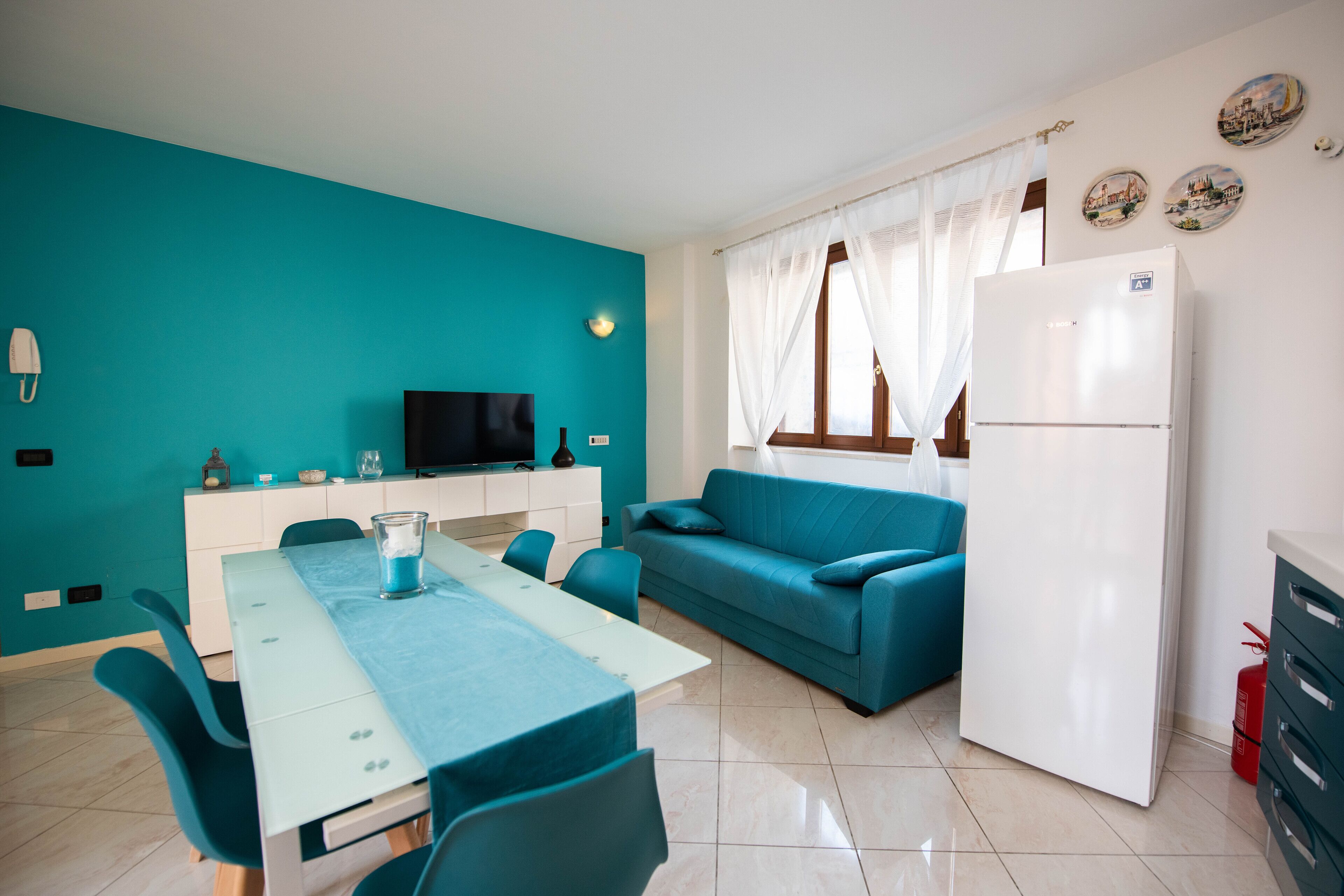Un soggiorno moderno con pareti color acquamarina, un frigorifero bianco, un divano blu e un'area pranzo con un tavolo e sedie in vetro.