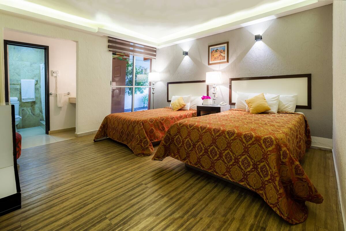 A hotel room with two beds, a bathroom, and a view of the outdoors.