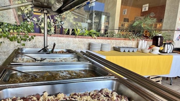 Un'area buffet con diverse postazioni, tra cui riso, un piatto a base di fagioli e uno con uova strapazzate.