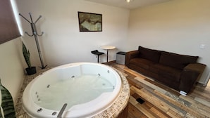 Un bagno con una vasca da bagno grande, un divano marrone, un tavolino e un quadro appeso al muro.