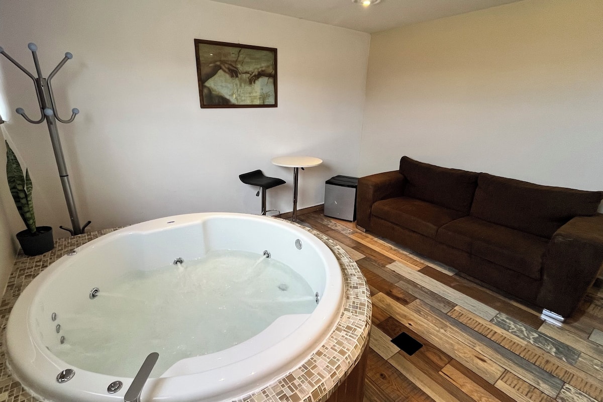 A bathroom with a large bathtub, a brown sofa, a small table, and a painting on the wall.