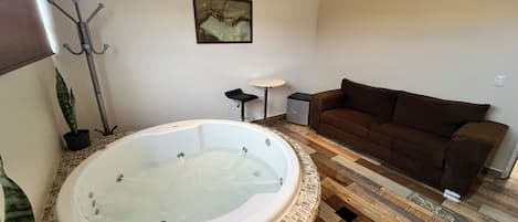 A bathroom with a large bathtub, a brown sofa, a small table, and a painting on the wall.