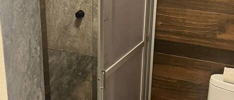 Una ducha a nivel con puerta de cristal, un cabezal de ducha y un inodoro en un baño con azulejos de mármol y madera.