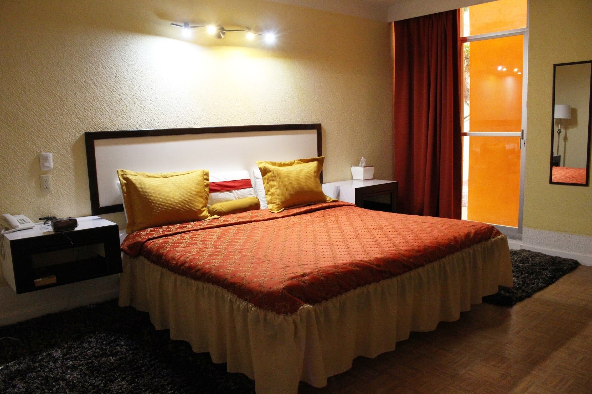 Una habitación de hotel con una cama grande, dos mesitas de noche, una lámpara de pared y una ventana con cortinas.