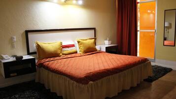 Una habitación de hotel con una cama grande, dos mesitas de noche, una lámpara de pared y una ventana con cortinas.