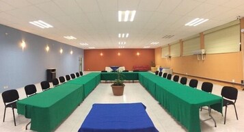 Un salón de conferencias con una larga mesa, sillas y una planta en maceta.