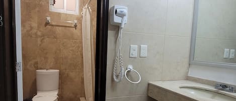 Un baño con inodoro, ducha, lavamanos y espejo.