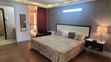 Habitación de hotel con cama, mesitas de noche, espejo, lámpara y vistas al exterior.