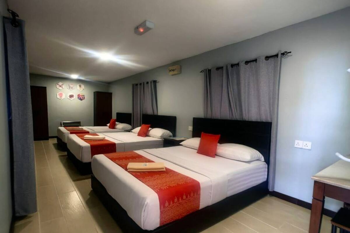 A hotel room with three beds, each with a red and white bedspread, and a small table with a chair.