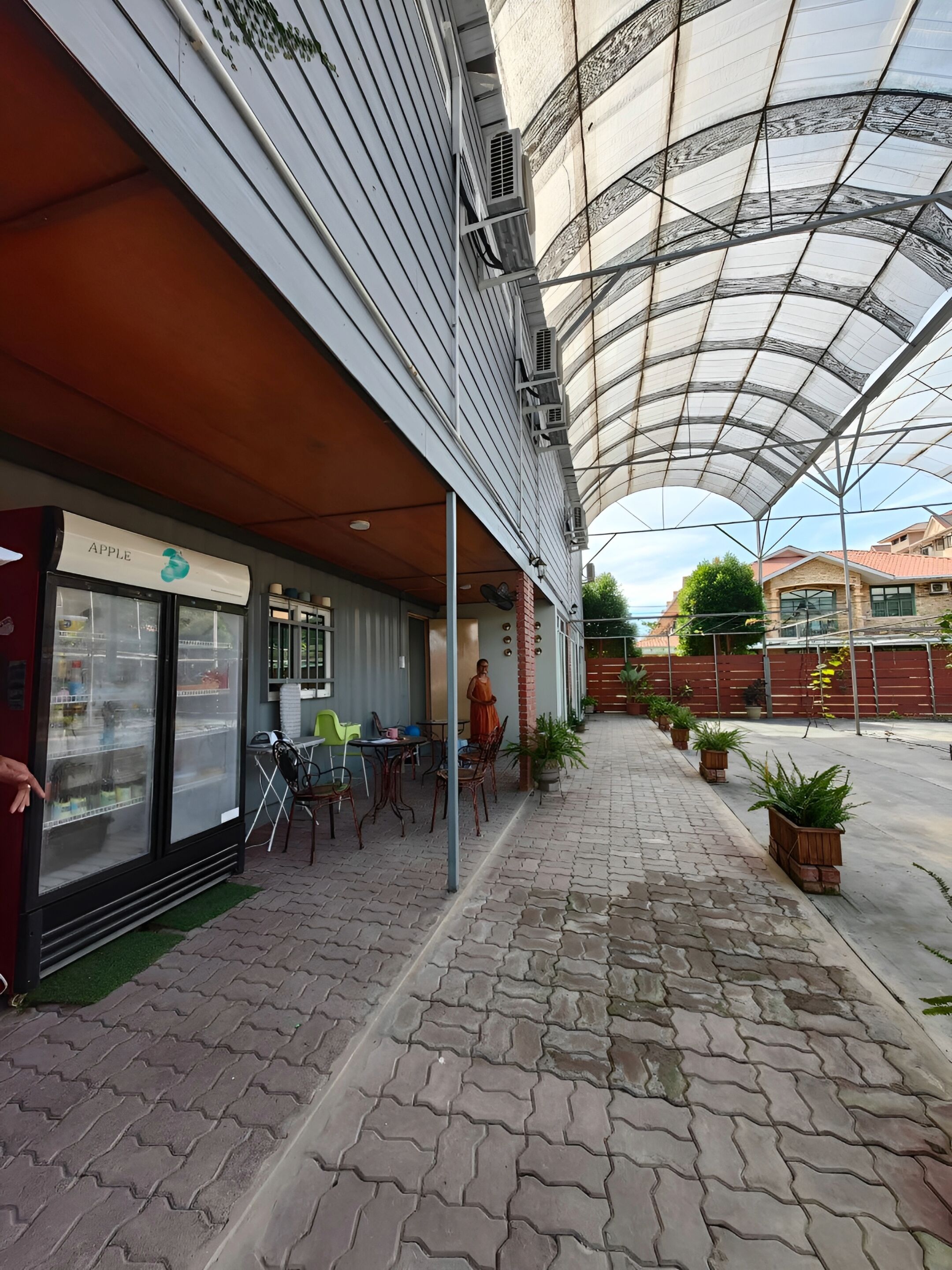 A covered outdoor area with a seating area, a refrigerator labeled "APPLE," and potted plants.
