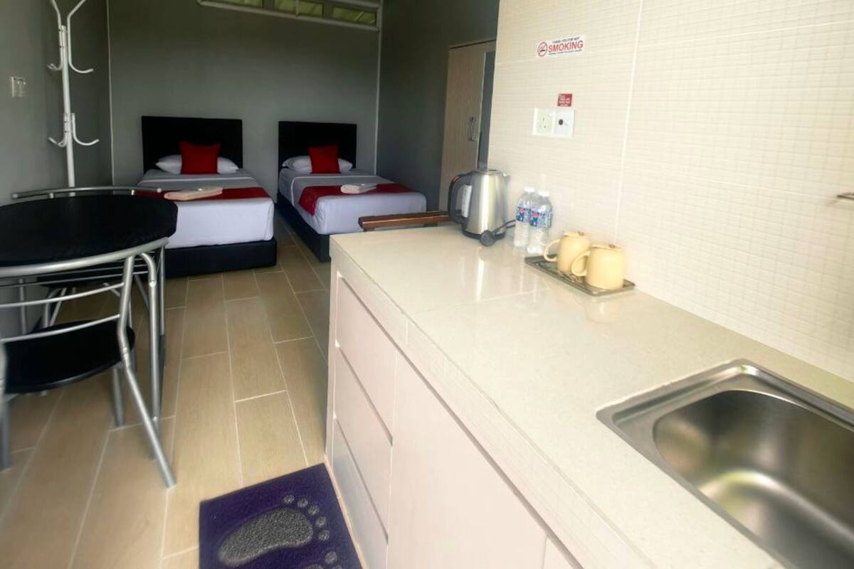 A compact hotel room with a kitchenette, two beds, a small dining table, and a ceiling fan.