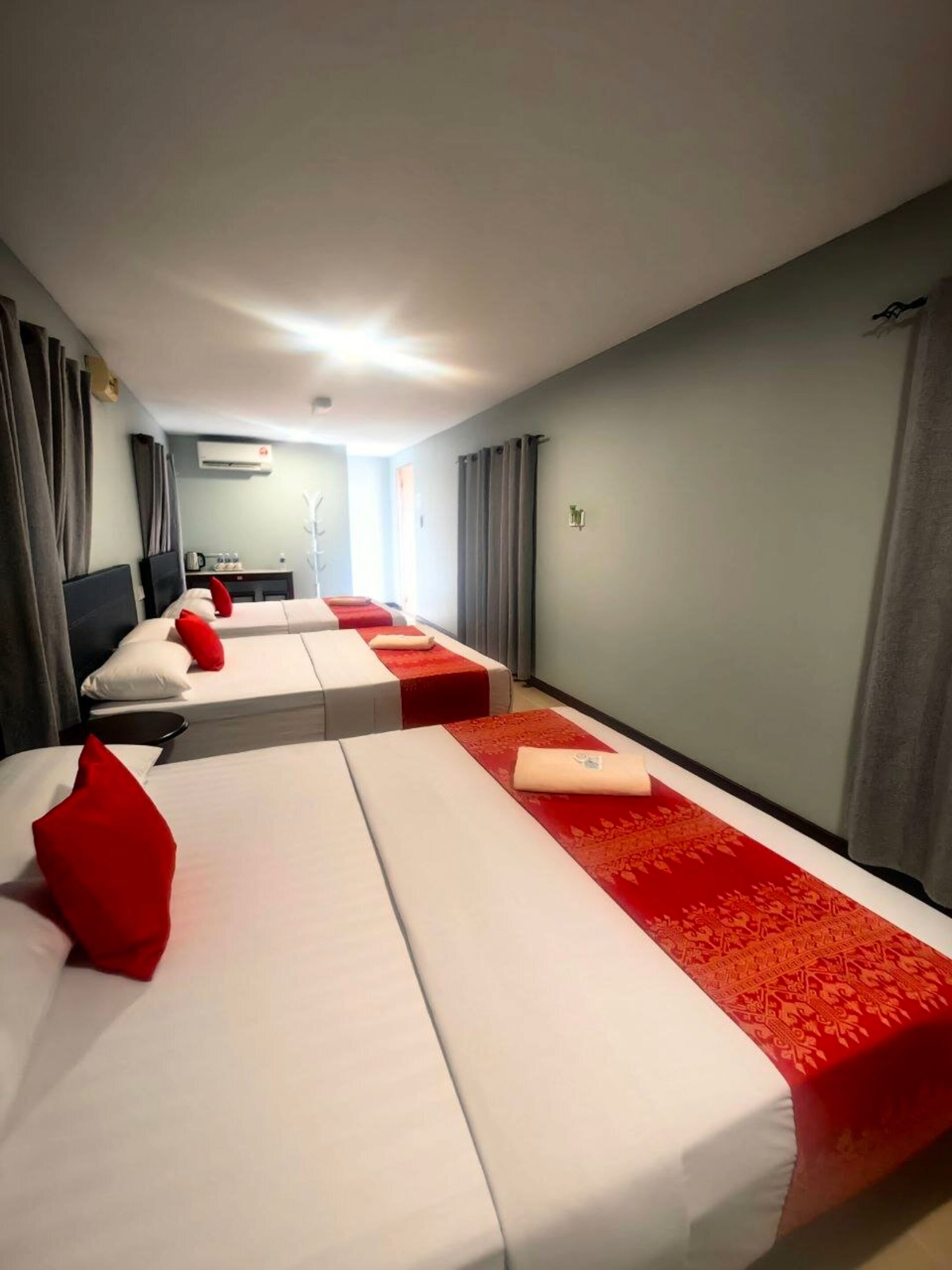 A hotel room with two beds, each with red and white bedding, a small table, and a wall-mounted air conditioner.