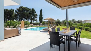 A covered patio with a pool, outdoor seating, and a table with chairs. - Ethria Pool Villa with heated jacuzzi (Αφάντου)