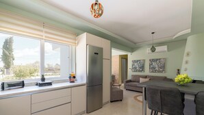 A modern kitchen with a refrigerator, dining area with chairs, and a window with blinds. - Ethria Pool Villa with heated jacuzzi (Αφάντου)