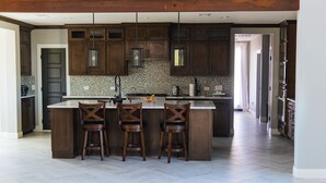 A modern kitchen with dark wooden cabinets, a large island with bar stools, and a tiled backsplash. - Large Modern home nestled in Alvarado! Hot Tub & Theater (Alvarado)