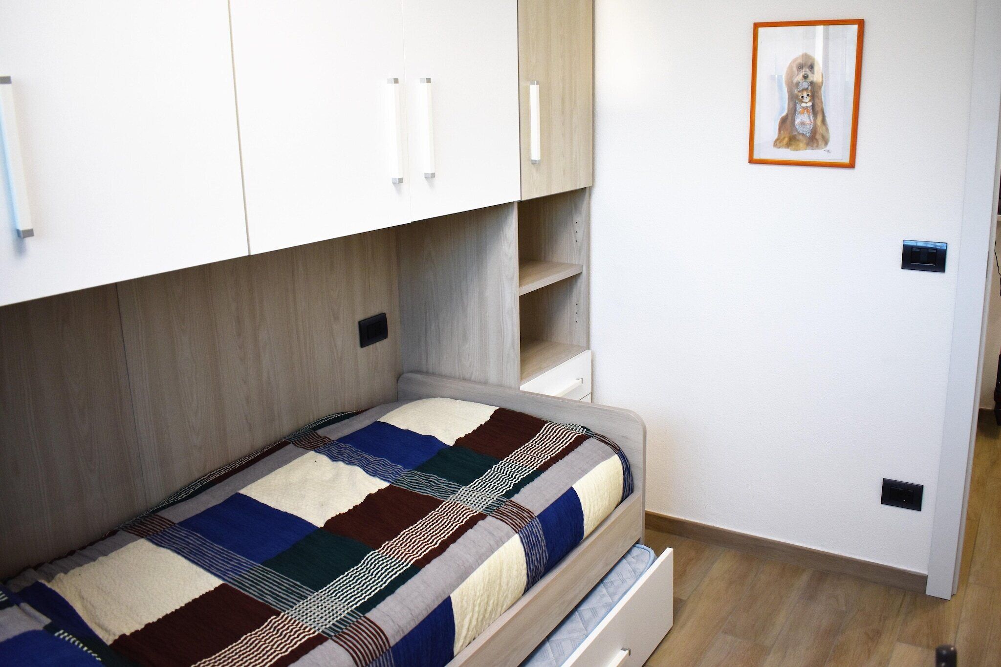 Een kleine kamer met een bed, een garderobe en een ingelijst schilderij aan de muur.