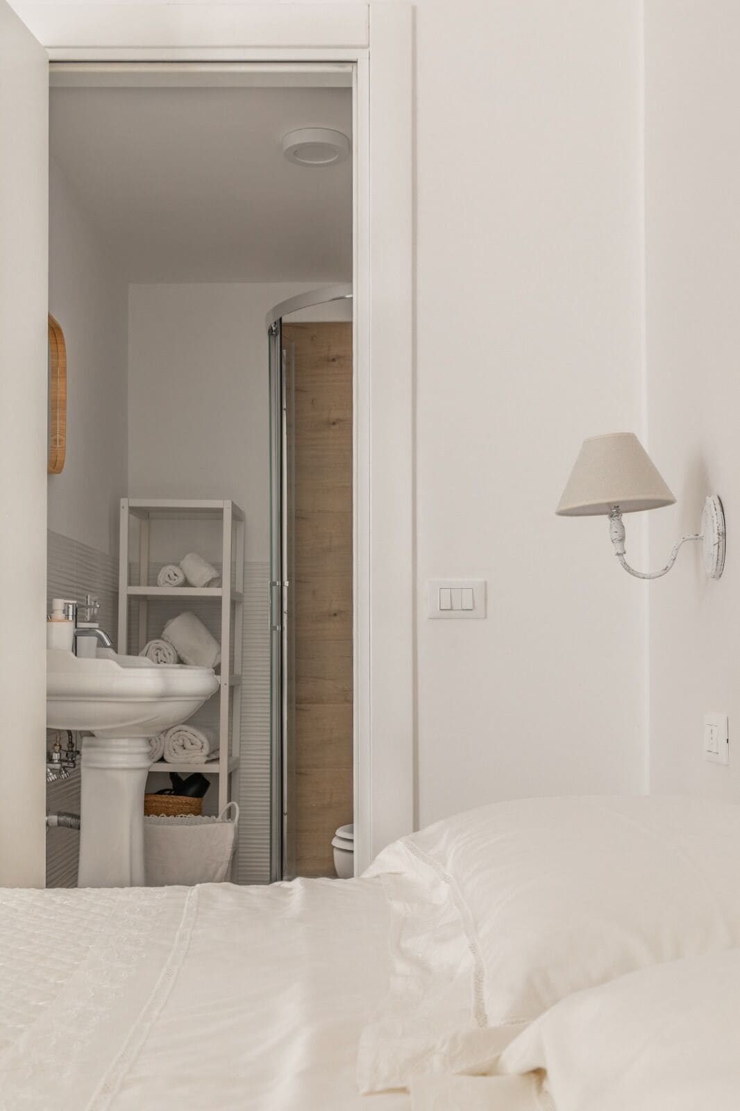 Un dormitorio con una cama, una lámpara blanca de pared, un lavabo blanco y una puerta de madera.