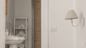Un dormitorio con una cama, una lámpara blanca de pared, un lavabo blanco y una puerta de madera.
