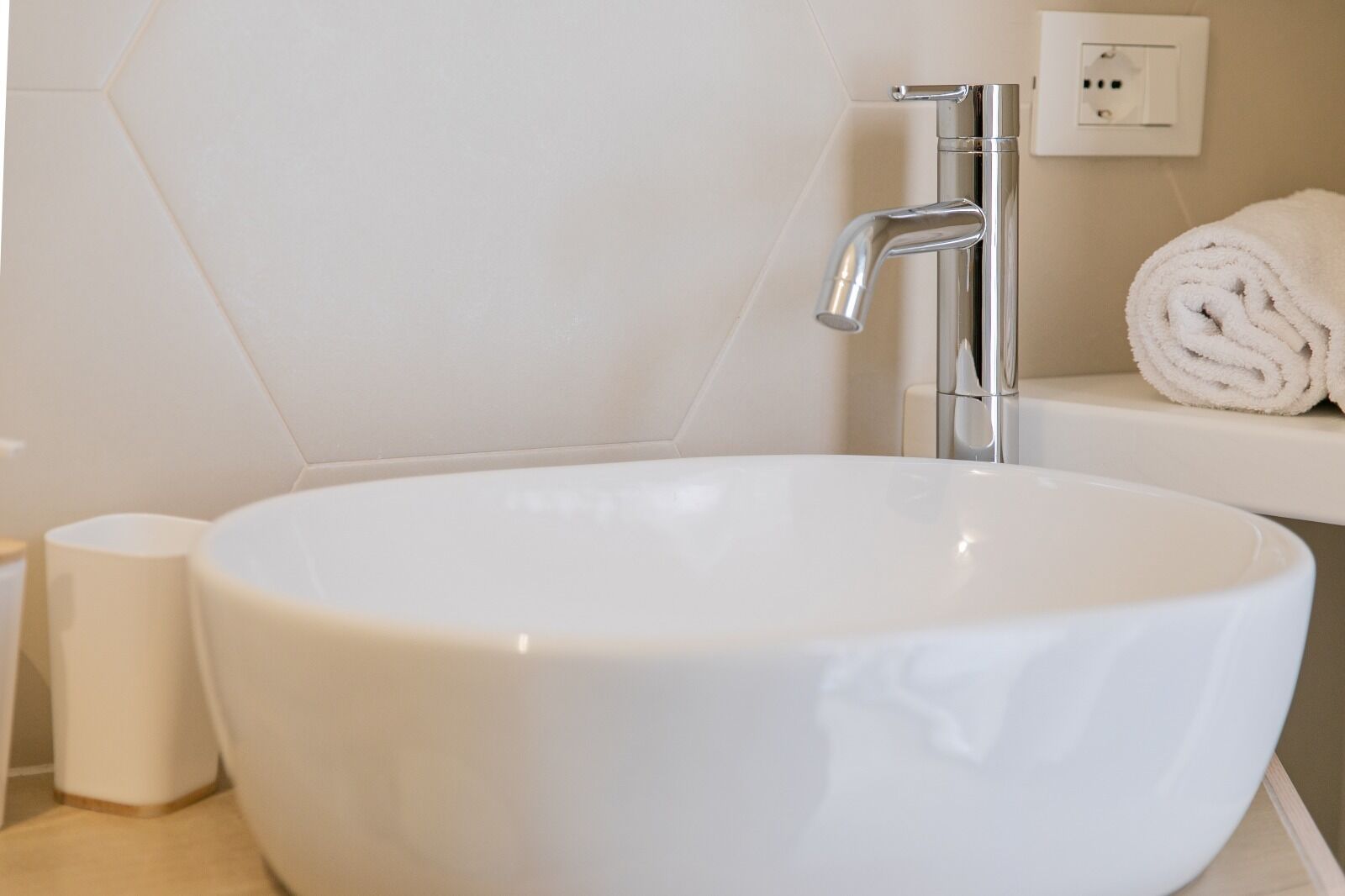 A white bathroom sink with a chrome faucet, a toilet paper holder, and a rolled towel on a shelf.