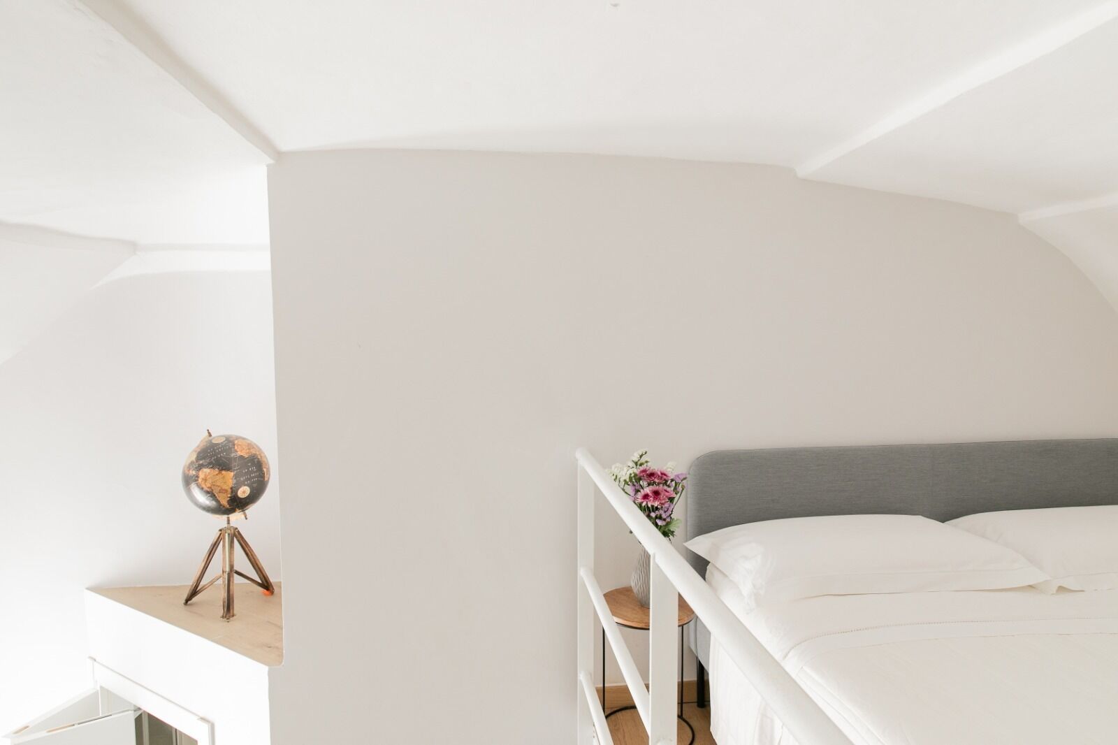 Ein schlicht eingerichtetes Schlafzimmer mit einem Etagenbett, einem kleinen Schreibtisch mit Globus und einer Blumenvase.