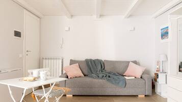 A modern living room with a grey sofa, a white table with a tray of bread, and a striped cushion.