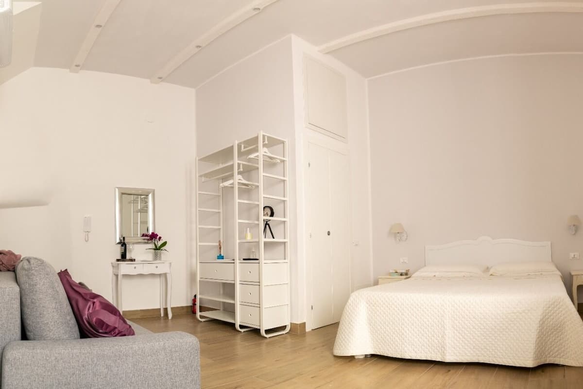 Un dormitorio con cama, un armario blanco, escritorio y televisor montado en la pared.