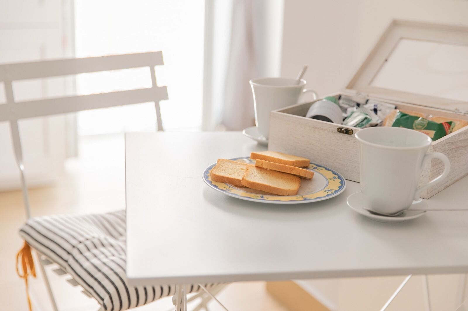 A breakfast setup with toast on a plate, a cup, and a box of tea on a white table.