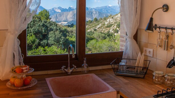 A kitchen with a view of mountains, a sink, and a fruit display.