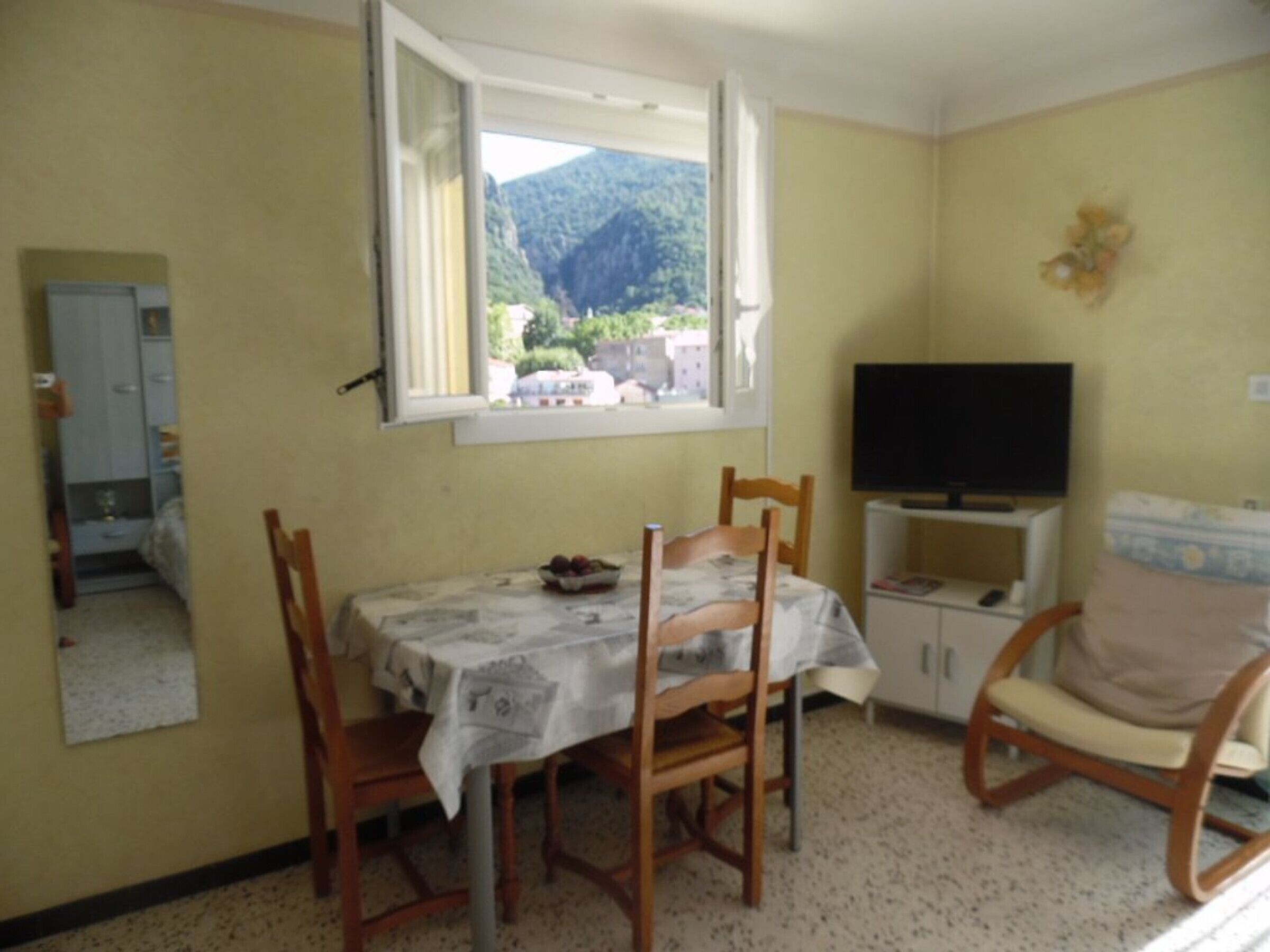A small dining area with a table, chairs, a television, and a window with a mountain view.