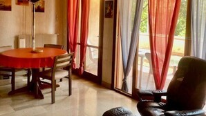 A room with a round table, chairs, a sofa, and a window with red and white curtains. - Bright F2 Apartment with Terrace, Parking, and WiFi in Amélie-les-Bains (Amélie-les-Bains-Palalda)